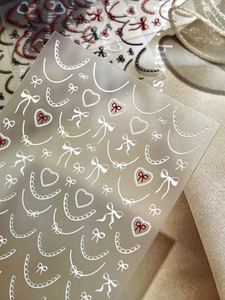 Detailed macro view of French lace nail stickers with white bows and red hearts