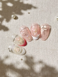 Close-up of pink tulip nail art with 3D bows and pearls on almond-shaped nails