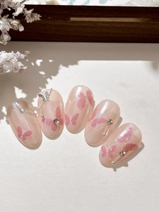 Gros plan d'ongles roses à coller avec breloques papillon, strass et motifs délicats