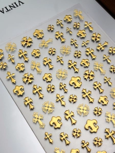 Détail de bijoux d'ongles métalliques dorés aux motifs de croix gothiques et lys
