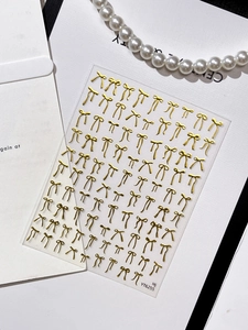 Macro detail of gold bow nail art stickers featuring metallic textures and pearl decor