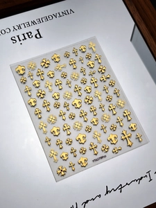 Gros plan de stickers à ongles croix et fleur de lys dorés mats sur fond vintage