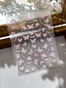 Détail de stickers à ongles papillon irisé rose avec strass sur un fond gris feutré