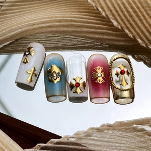 Nail art style gothique avec croix dorée, fleur de lys et strass sur base miroir