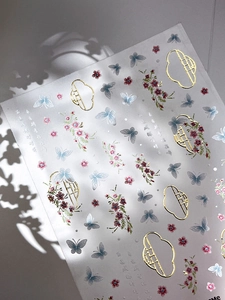 Detail of gold foil butterfly nail stickers with delicate blue floral patterns