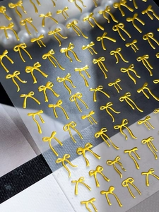 Macro detail of 3D embossed gold bow nail art stickers with metallic relief texture