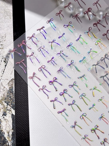 Detailed macro view of 3D laser bow nail art stickers with iridescent rainbow finish