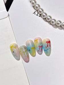 Detail of gradient almond press-on nails featuring 3D bows, stars and sparkling rhinestones