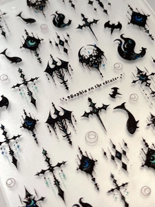 Close-up of 3D gothic nail stickers featuring black cross, moon, and star embossed patterns