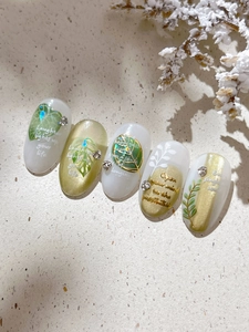 Detailed view of press-on nails featuring green leaves and gold letter stickers