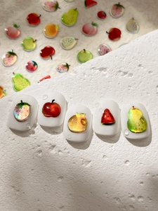 Macro shot of 3D fruit nail stickers with strawberry and orange designs on white tips