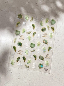 Macro shot of green botanical nail stickers with gold accents and leaves on marble background