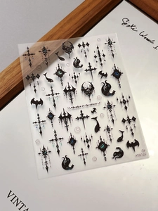 Detail of gothic nail stickers with black cross, eye, and bat motifs on a white background