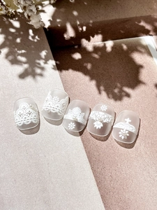 Detail of matte press-on nails featuring white lace patterns and delicate 3D pearl accents