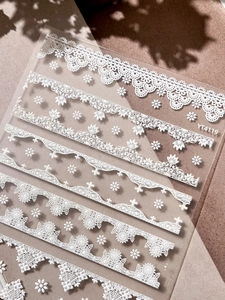Close-up of white embossed lace nail stickers with floral patterns on transparent backing