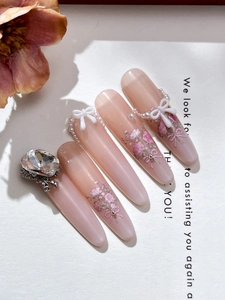 Macro detail of handmade nail tips with resin bows, pearls and floral textures