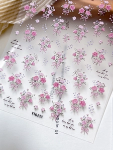 Macro view of 3D embossed nail stickers featuring pink roses and purple bows on white
