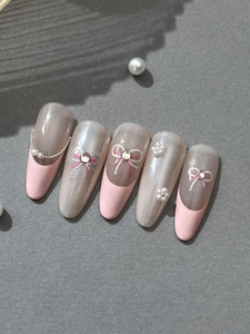 Detail of pink almond fake nails with pearl flowers and sparkling rhinestone bows