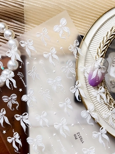 Detailed view of 3D white ribbon bow nail stickers with elegant pearl background