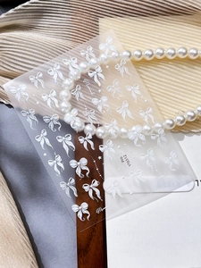 Macro detail of 3D embossed white ribbon bow nail stickers with pearl background