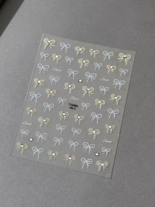 Close-up of light blue and gold bow nail stickers with sparkling crystal diamond effects