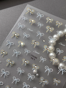 Detailed view of blue and gold bow nail stickers with rhinestones on grey background