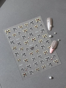 Macro detail of bow nail stickers with gold accents and rhinestones on soft pink nails