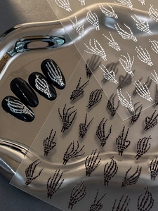 Detail of 3D skeleton hand nail stickers on black nails and silver metallic display tray