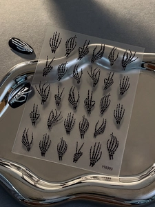 Detail view of black skull hand nail art stickers with diverse gestures on a silver tray