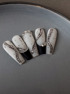 Detail of long coffin nails with black ink splashes and silver spine 3D texture charms