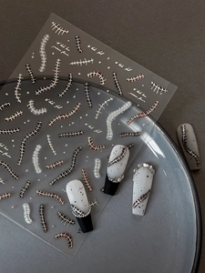 Macro detail of metallic silver fishbone and spine nail art stickers on a white surface