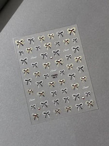 Detail of bow-knot nail stickers with gold edges and crystal rhinestones on dark background