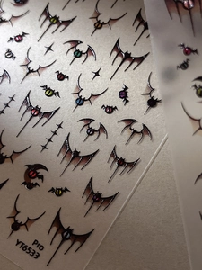 Macro detail of Gothic bat wings and colorful eyeball 3D nail art stickers on card