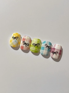 Detailed view of colorful plaid nail art tips with black bow designs in five vibrant shades