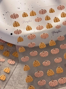 Macro detail of 3D embossed pumpkin nail art stickers in muted pink and mustard yellow tones