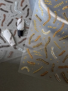 Detail showing 3D embossed spine pattern nail stickers with metallic textures and studs