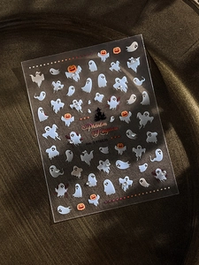 Macro detail of Halloween nail stickers featuring white ghosts and pumpkins on clear film