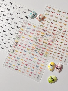 Detail of 3D embossed bow nail art stickers in various colors applied on plaid manicures