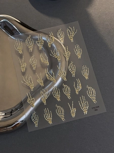 Detail of gold skeleton hand nail stickers for Halloween with metallic embossed texture