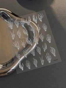 Macro shot of Halloween skeleton hand nail stickers on dark background with silver ring decor