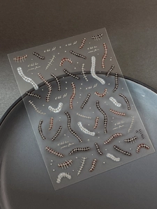 Macro shot of dark-style nail art stickers with bone and ribbon patterns on a ceramic plate