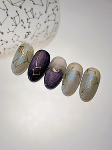 Detail of zodiac nail stickers with golden constellations on purple cat eye nails
