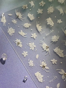 Macro detail of white embossed flower and butterfly nail stickers with tiny rhinestones