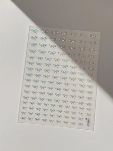 Macro shot of 3D laser silver bow nail art stickers with metallic reflective details
