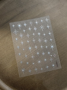 Detailed view of silver starburst nail stickers with rhinestone accents on clear film