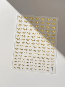 Close-up of golden bow nail stickers with metallic relief texture on white background