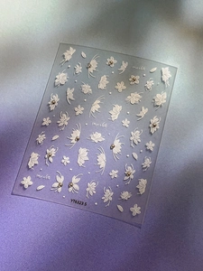 Detail of white embossed floral and butterfly nail stickers on purple background