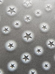 Macro shot of grey nail stickers featuring embossed star patterns and matte texture