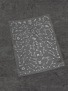 Macro detail of metallic silver zodiac sign nail stickers with constellations on dark stone
