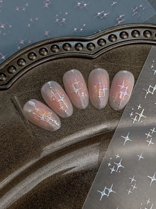 Macro detail of holographic cross star nail stickers on soft pink manicured nails